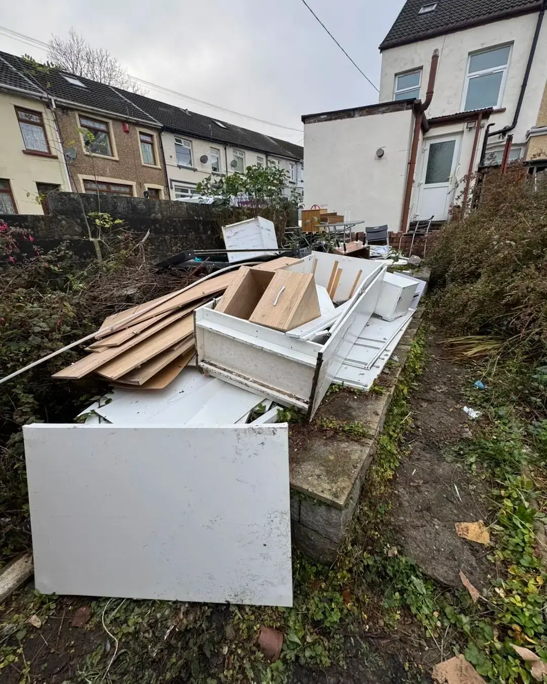 Dismantled wardrobes and drawers in a terraced back garden, ready for a house clearance